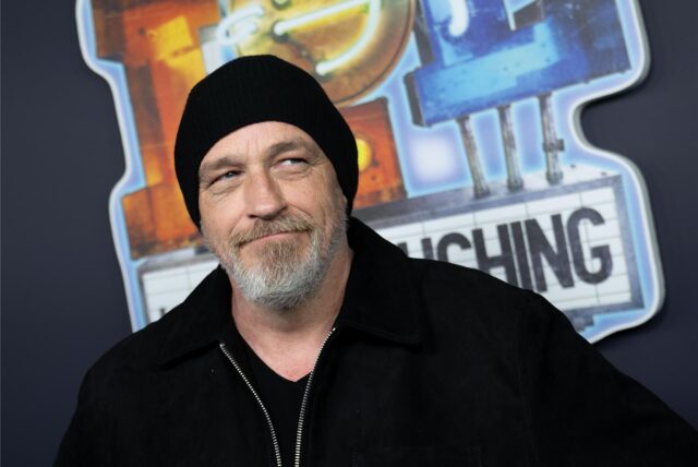 Comedian Torsten Sträter steht vor dem Plakat der Serie „LOL – Last One Laughing“.