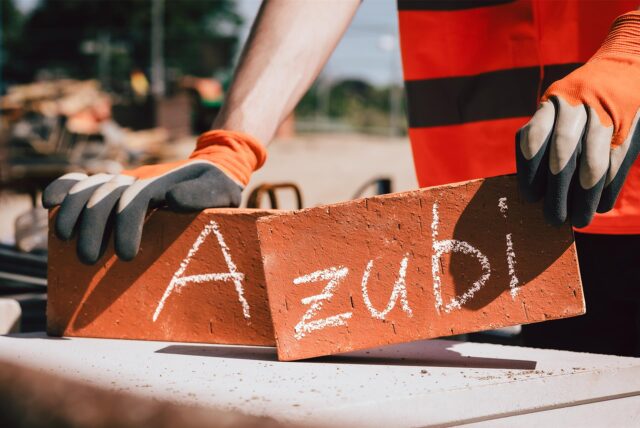 Das Wort „Azubi“ ist mit Kreide auf zwei Backsteine geschrieben. Eine Person hält die Steine mit seinen Händen fest.