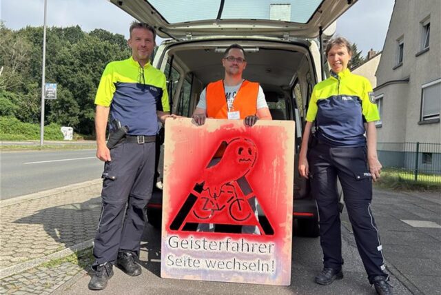 Drei Menschen, die hinter einem Warnlogo stehen.