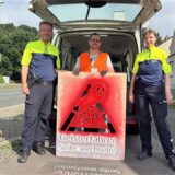 Drei Menschen, die hinter einem Warnlogo stehen.