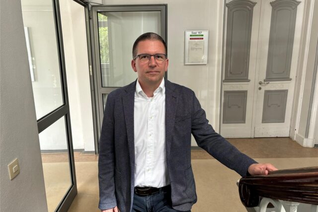 Lutz Grimm, Direktor des Amtsgerichts Recklinghausen, steht in einem Treppenhaus des Altbaus des Amtsgerichts an der Reitzensteinstraße und legt eine Hand auf das Treppengeländer aus Holz.