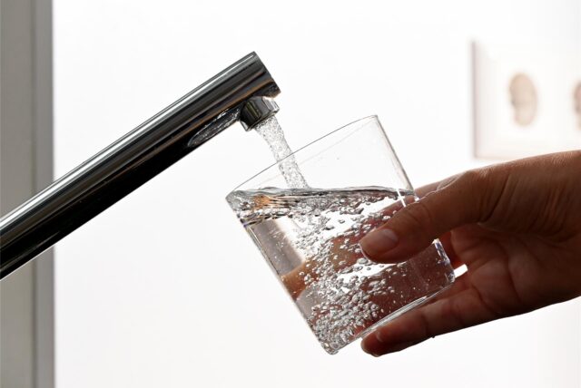 Eine Person hält ein Glas Wasser unter einen Wasserhahn und lässt es voll laufen (Symbolbild).