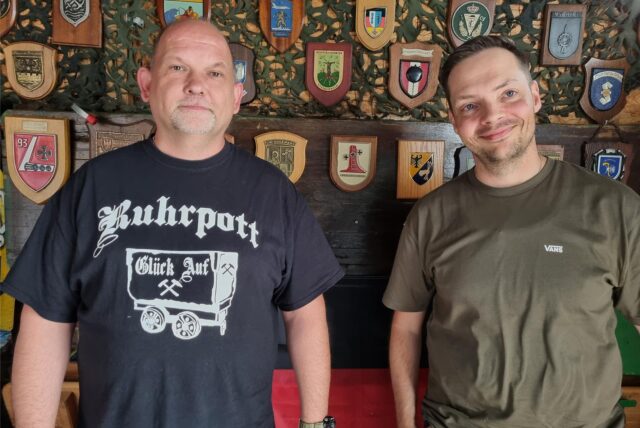 Zwei Männer stehen vor einer Wand.