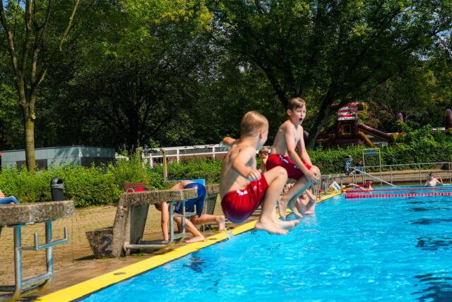 Zwei Kinder springen mit einer Arschbombe ins Wasser im Freibad Mollbeck in Recklinghausen.