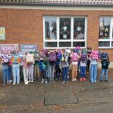 Mehrere Kinder stehen an einer Wand und halten sich ihre Tornister vor ihre Gesichter.