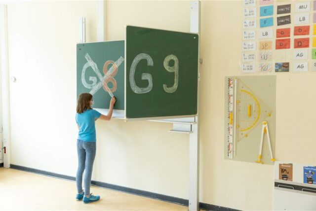 Ein Mädchen steht an einer Tafel, auf der groß G8 und G9 geschrieben stehen, und streich G8 durch.