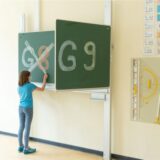 Ein Mädchen steht an einer Tafel, auf der groß G8 und G9 geschrieben stehen, und streich G8 durch.