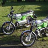 Zwei Mopeds stehen auf einer Wiese. Bei den Mopeds handelt es sich um zwei Modelle der Firma Kreidler. Eins ist eine Kreidler Florett RS, das andere eine Kreidler Florett RMC. Sie sind beide in einem hellgrünen Farbton lackiert.