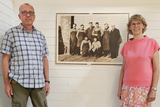 Markus Rath und Susanne Rath-Peters stehen vor einem schwarz-weißen Foto an einer Wand.