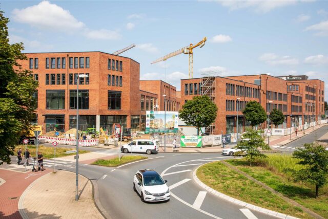 Die Baustelle der Hertener Höfe. Rechts davor ist der Kreisverkehr in Herten-Mitte zu sehen, durch den ein weißes Auto fährt.