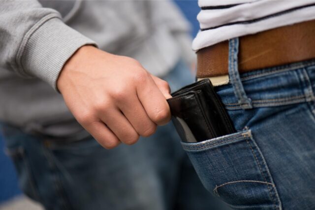 Ein Mann zieht einem anderen das Portemonnaie aus der Gesäßtasche einer Jeans.