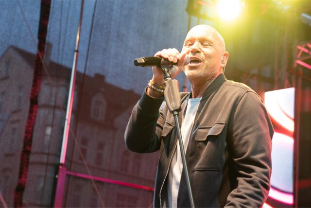 Schlagersänger Olaf Henning steht auf einer Bühne, hält ein Mikrofon in seiner rechten Hand und singt.