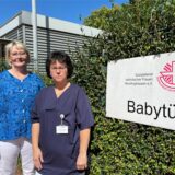 Andrea Korte-Toffel, Sozialpädagogin beim SkF Recklinghausen (links), und Susanne Kwiatkowski, Leiterin der geburtshilflichen Station im Prosper-Hospital, stehen neben einem Schild mit der Aufschrift Babytür.
