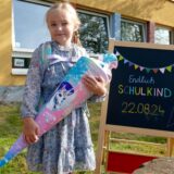 Anne Sophie seht an der Süder Grundschule in Herten neben einer Tafel, auf dem steht, dass sie endlich Schulkind ist, versehen mit dem Datum ihrer Einschulung.