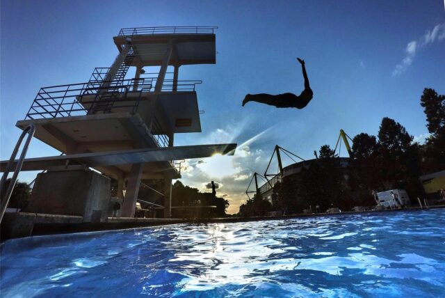 Ein Mann springt im Freibad Volkspark in Dortmund vom Sprungturm ins Schwimmbecken.