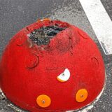 Ein roter Pömpel auf einer asphaltierten Straße. Oben ist eine massive Schramme zu erkennen.