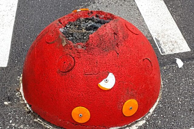 Ein roter Pömpel auf einer asphaltierten Straße. Oben ist eine massive Schramme zu erkennen.