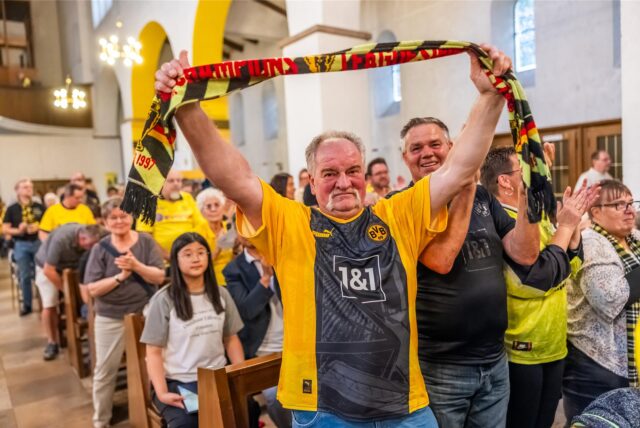 Ein Fan im BVB-Trikot hält in der Kirche einen Schal hoch.
