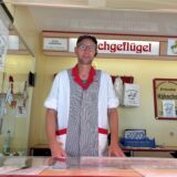 Matthias Kortmann steht an der Theke seines Fleischwagens auf dem Hertener Markt. Im Hintergrund sind Angebotsschilder an die Wand des Verkaufsstandes gehängt. Kortmann trägt eine Metzger Uniform.