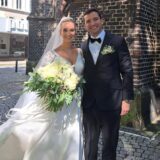 Strahlendes junges Brautpaar, sie in Weiß und er im schwarzen Anzug, vor der Antonius-Kirche in Herten.