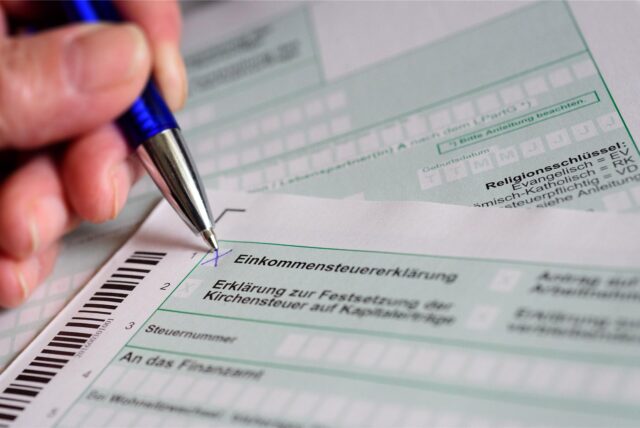 Eine Hand mit Kugelschreiber setzt ein Kreuz bei „Einkommensteuererklärung“ auf dem offiziellen Formular des Finanzamts.