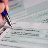 Eine Hand mit Kugelschreiber setzt ein Kreuz bei „Einkommensteuererklärung“ auf dem offiziellen Formular des Finanzamts.