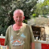 Ein Mann mit weit geschnittenem T-Shirt steht vor einer Baustelle. Der Gehweg hinter ihm ist aufgerissen und mit Baken abgesperrt.