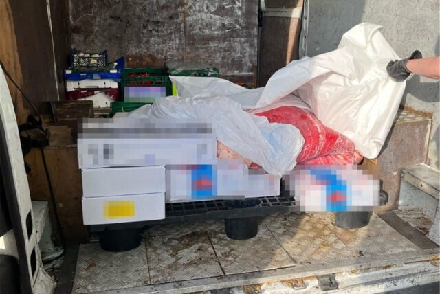 Die Ladefläche eines Transporters, in der sich Kisten befinden, die verpixelt sind. Eine Hand hält eine weiße Plastikplane nach oben, unter der sich ein Plastiksack befindet.