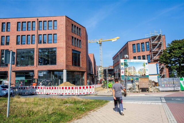 Die Baustelle der Hertener Höfe. Über einen Fußgängerüberweg, der zur Baustelle führt, geht gerade ein Mann in Arbeitskleidung.