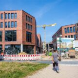 Die Baustelle der Hertener Höfe. Über einen Fußgängerüberweg, der zur Baustelle führt, geht gerade ein Mann in Arbeitskleidung.