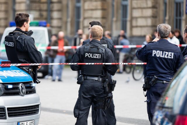 Einsatzkräfte der Polizei stehen vor einem Bahnhof in einer abgesperrten Zone.