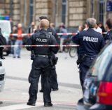 Einsatzkräfte der Polizei stehen vor einem Bahnhof in einer abgesperrten Zone.