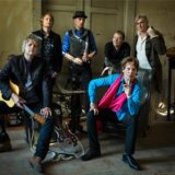 Die Rolling-Stones-Cover-Band „Voodoo Lounge“ posiert mit ihren Instrumenten in einem alten Gebäude vor einer alten Tür.