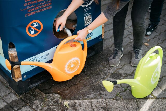 Gießkannen werden an einem Regenwassertank befüllt.