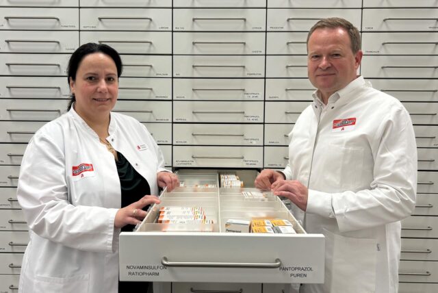Apothekerin Irini Zervas und MdB Frank Schwabe (SPD) stehen vor einer ausgezogenen Schublade eines Medikamentenschranks in der Quellberg-Apotheke in Recklinghausen. Beide tragen einen weißen Kittel.