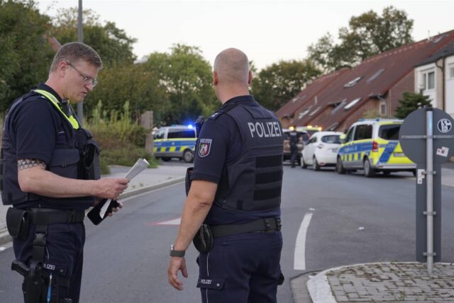 Zwei uniformierte Polizisten stehen auf einer Straße in Recklinghausen. Im Hintergrund sind Einsatzwagen zu sehen.