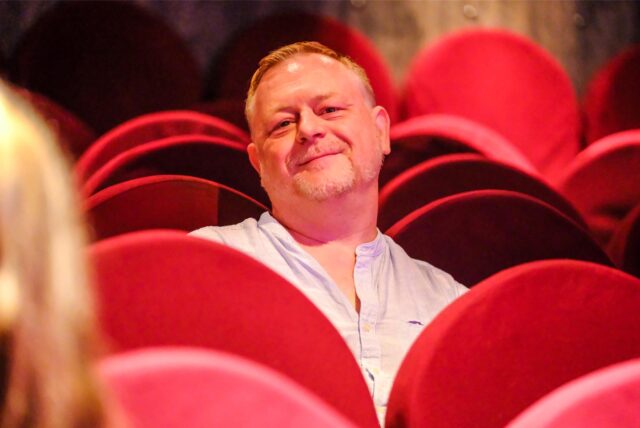 Ein Mann sitzt in einer Reihe mit roten Sitzen