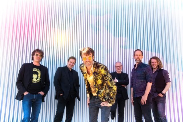 Bastian Korn steht inmitten seiner Band vor einer Wand.