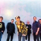 Bastian Korn steht inmitten seiner Band vor einer Wand.