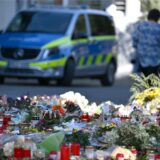 Blumen und Kerzen liegen auf einem Marktplatz. Im Hintergrund ist ein Polizeiauto zu sehen.