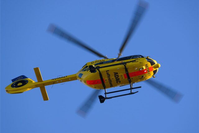 Ein gelber Rettungshubschrauber der ADAC fliegt am blauen Himmel entlang.