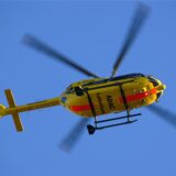 Ein gelber Rettungshubschrauber der ADAC fliegt am blauen Himmel entlang.