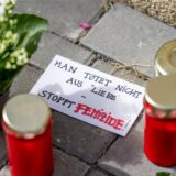 Blumen und Kerzen liegen vor einem Hauseingang neben einem Zettel mit der Aufschrift „Man tötet nicht aus Liebe – Stoppt Femizide“.