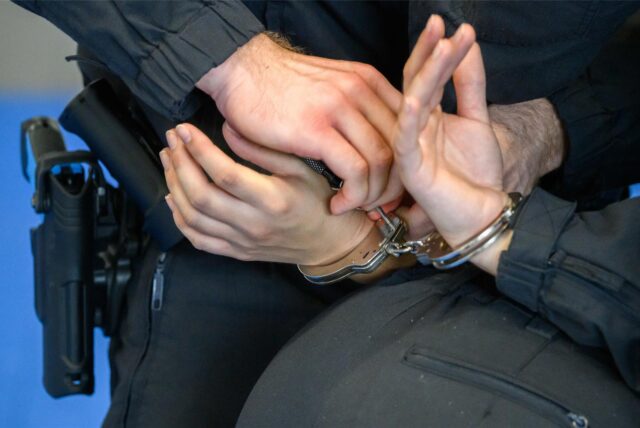 Nahaufnahme von zwei Polizisten-Händen, die Handschellen bei einer anderen Person anlegen.