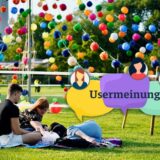 Drei Menschen sitzen oder liegen auf der Wiese im Westfalenpark. Im Hintergrund hängen viele bunte Lampions.