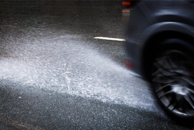 Wasser auf einer Straße spritzt hinter einem Fahrzeug hoch.