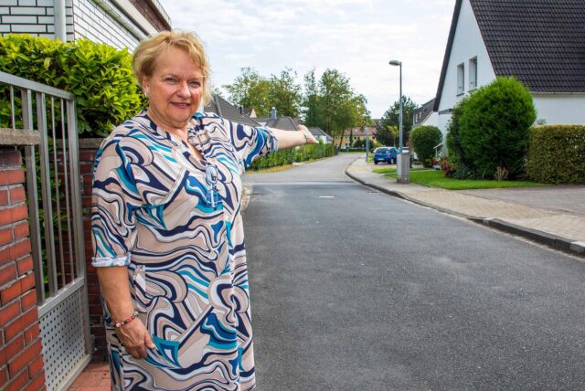 Petra Herold steht am Erich-Grisar-Weg in Herten-Süd und deutet mit dem linken Arm die Straße herunter.