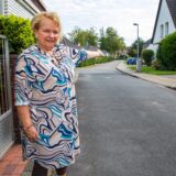 Petra Herold steht am Erich-Grisar-Weg in Herten-Süd und deutet mit dem linken Arm die Straße herunter.