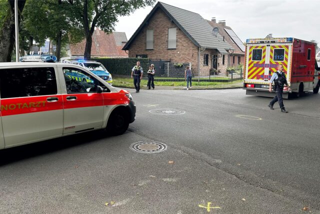 Ein Rettungswagen und ein Notarzt-Einsatzfahrzeug stehen auf einer Straße. Polizisten schauen sich die Unfallspuren an.