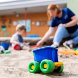 Symbolbild einer Erzieherin, die mit einem Kind im Sandkasten spielt